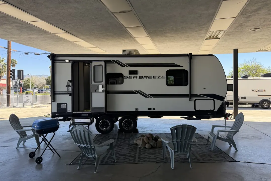 A 2023 Genesis Supreme Sea Breeze travel trailer staged under a canopy with chairs set out