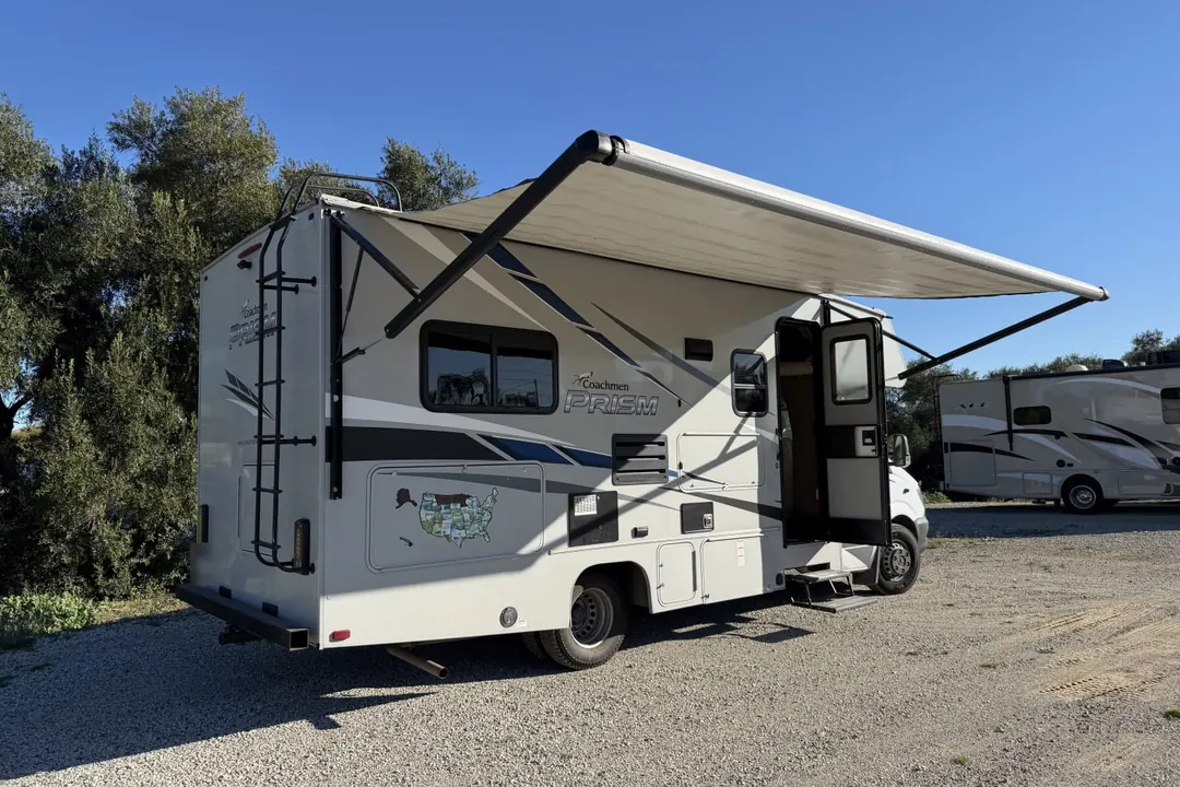 A 2020 Coachmen Prism motorhome with its awning out on a gravel lot