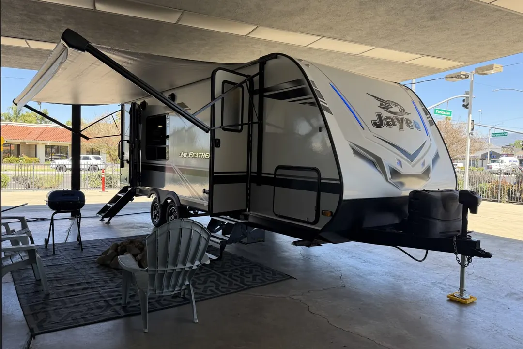 A 2021 Jayco Jay Feather with its awning out, chairs and a rug set up beside it